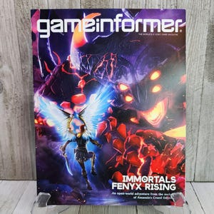 May include: A magazine cover for Game Informer featuring the video game Immortals Fenyx Rising. The cover art depicts a winged female character with a sword, facing a large, menacing, red-eyed creature with glowing orange eyes.