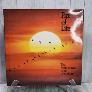 May include: A book cover depicting a sunset scene with a flock of birds flying in formation. The title "Fire of Life" is printed in black text at the top of the cover. The text "The Smithsonian Book of the Sun" is printed in black text at the bottom of the cover.