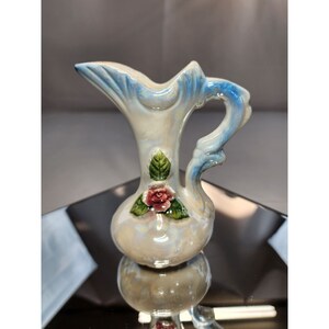 May include: A small, white ceramic pitcher with a blue and white glaze. It has a floral design with a pink rose and green leaves.