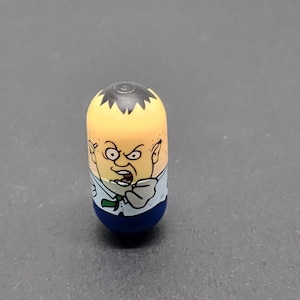 May include: A small, blue and yellow plastic toy with a cartoon face. The toy has black hair and a white shirt with a green tie. The toy is a character from the popular cartoon series, "The Amazing World of Gumball."