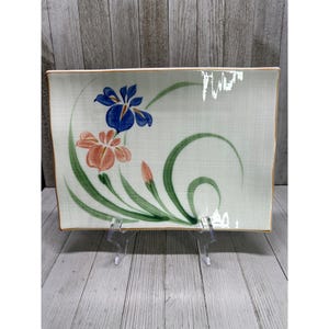 Puede incluir: Plato rectangular de cerámica con fondo verde claro y diseño floral. Las flores son azules y melocotón con hojas y tallos verdes. Los bordes están ribeteados en color dorado.