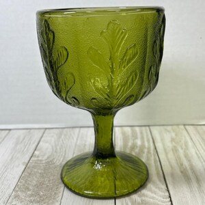 May include: A green glass goblet with a floral design. The goblet has a wide bowl and a tall stem.