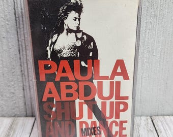 May include: A cassette tape with a black and white photo of Paula Abdul on the front. The text "Paula Abdul Shut Up And Dance Mixes" is printed in red and white.