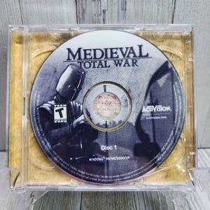 May include: A CD case with a disc inside. The disc is labeled "Medieval Total War" and features a knight in armor. The case is labeled "Disc 1" and includes the text "Windows 98/ME/2000/XP".