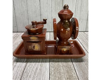 Könnte beinhalten: Ein braunes Keramik-Salz- und Pfefferstreuer-Set in Form von Kaffeemühlen. Die Mühlen stehen auf einem passenden braunen Tablett. Der Salzstreuer hat ein "S" und der Pfefferstreuer ein "P" darauf.