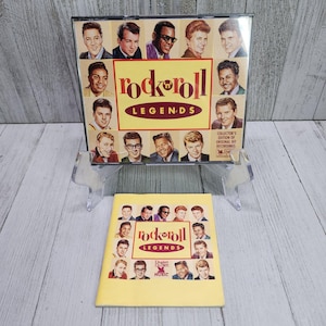 Puede incluir: Una caja de CD amarilla con un collage de 16 caras de hombres en la parte delantera. El texto "Rock 'n' Roll Legends" está impreso en letras rojas y negras. La caja está en un soporte de plástico transparente. También se muestra un folleto amarillo con el mismo título y un collage de caras similar.