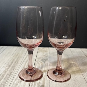 Op de afbeelding: Twee heldere roze wijnglazen met een delicaat gegraveerd ontwerp. De glazen hebben een hoge steel en een ronde kom.