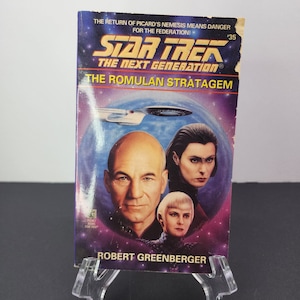 May include: A Star Trek: The Next Generation paperback book cover featuring a blue and purple space background with a starship, a portrait of Captain Jean-Luc Picard, and the title "The Romulan Stratagem".