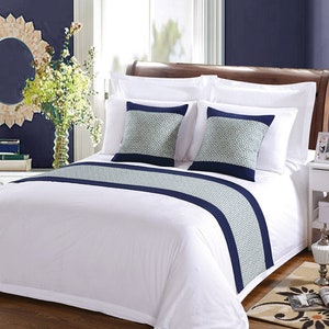 May include: White bed with a navy blue and white patterned bed runner and two matching decorative pillows. The bed is made with white sheets and a white duvet cover.