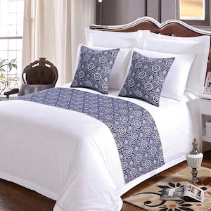 May include: White bed with a blue and white patterned bed runner and two matching throw pillows. The bed is made with white sheets and a white duvet cover. The bed is in a bedroom with a white nightstand and a lamp.