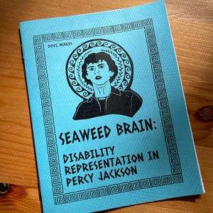 May include: A blue booklet with a black border and a Greek key pattern. The cover features a black and white illustration of a person with curly hair, wearing a black shirt and a necklace. The text on the cover reads "Seaweed Brain: Disability Representation in Percy Jackson" and "Dove Makes".