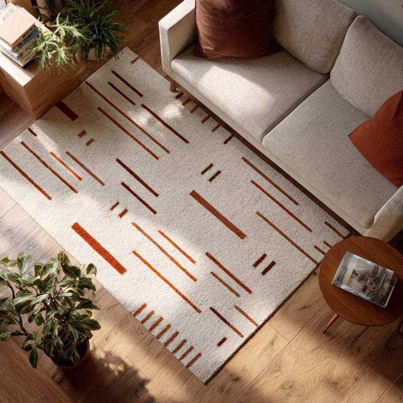 May include: A rectangular area rug with a cream-colored background and a pattern of rust-colored lines. The lines vary in length and are arranged in a scattered, geometric design. The rug is placed on a hardwood floor.