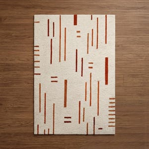 May include: Rectangular off-white rug with a repeating pattern of vertical and horizontal rust-colored lines. The rug is placed on a wooden floor. The design is modern and geometric, suitable for a living room or bedroom.