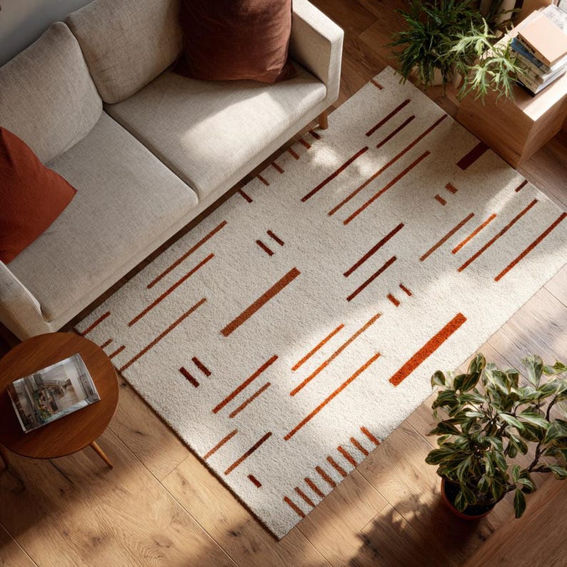 May include: An overhead view of a living room featuring a cream-colored sofa, a round wooden side table, and a rectangular rug. The rug has a cream background with a pattern of brown rectangular and linear shapes. Potted plants and a wooden storage unit are also visible.