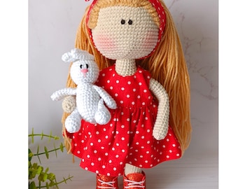 May include: A handmade crochet doll with long blonde hair, wearing a red polka dot dress, red glitter shoes, and a red headband. The doll is holding a small white crochet bunny. The doll's face is beige with black eyes and rosy cheeks.