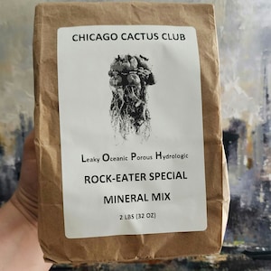 Puede incluir: Una bolsa de papel marrón con una etiqueta blanca que dice "CHICAGO CACTUS CLUB" y "ROCK-EATER SPECIAL MINERAL MIX 2 LBS (32 OZ)". La etiqueta también tiene una ilustración en blanco y negro de un cactus.