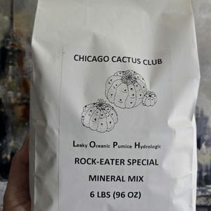 Op de afbeelding: Een witte papieren zak met de tekst "CHICAGO CACTUS CLUB" en een cactusillustratie. De zak bevat "ROCK-EATER SPECIAL MINERAL MIX" en weegt 2,72 kg. De tekst bevat ook "Leaky Oceanic Pumice Hydrologic."