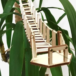 Op de afbeelding: Een houten model van een hangbrug met een touw leuning en een houten dek. De brug is gemaakt van lichtbruin hout en heeft een natuurlijke afwerking.