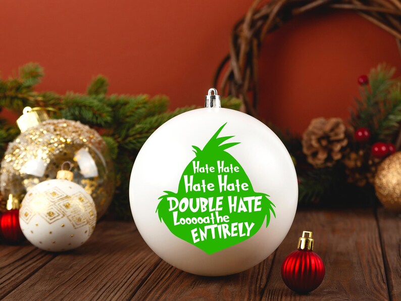 May include: White Christmas ornament with a green Grinch design and the text "Hate Hate Hate Hate Double Hate Looooathe Entirely". The ornament is surrounded by other Christmas decorations.