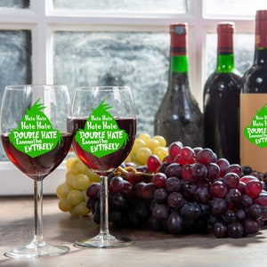 May include: Two wine glasses filled with red wine, each with the text "Hate Hate Hate Hate DOUBLE HATE Looooathe ENTIRELY" in green. The glasses are next to grapes and wine bottles.