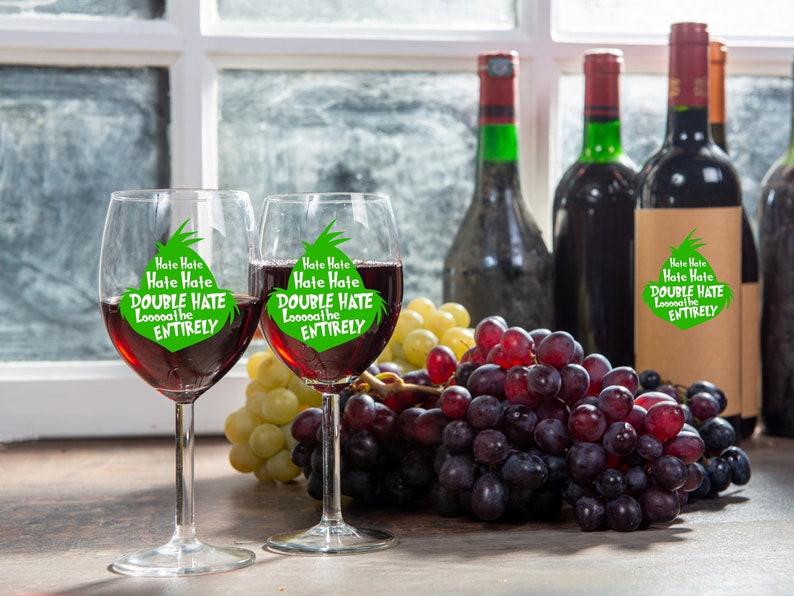 May include: Two wine glasses filled with red wine, each with the text "Hate Hate Hate Hate DOUBLE HATE Looooathe ENTIRELY" in green. The glasses are next to grapes and wine bottles.