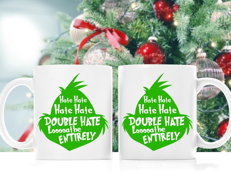 May include: Two white ceramic mugs with a green graphic of a character's face and the text "Hate Hate, Hate Hate, DOUBLE HATE, Looooathe, ENTIRELY". The mugs are in front of a Christmas tree.