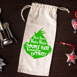 May include: A canvas wine bag with a green graphic and the text "Hate Hate Hate Hate DOUBLE HATE Loooooathe ENTIRELY". A silver corkscrew and Christmas ornaments are also in the image.