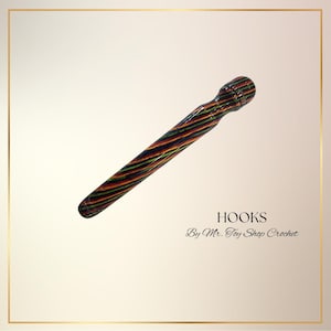 May include: A colorful crochet hook with a striped pattern in shades of red, yellow, green, and blue. The hook is labeled "HOOKS" and "By Mr. Toy Shop Crochet".
