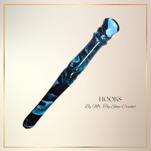 May include: A crochet hook with a marbled design in shades of blue and black. The hook has a rounded top and a tapered shaft. Text on the image reads "HOOKS By Mr. Toy Shop Crochet."