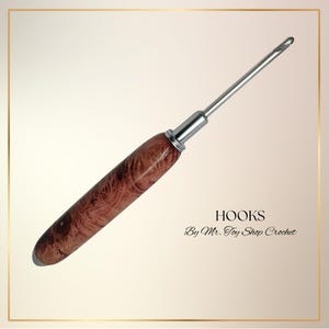 May include: A crochet hook with a polished, wooden handle and a silver metal hook. The handle has a rich, reddish-brown color with a unique wood grain pattern. The text "HOOKS By Mr. Toy Shop Crochet" is visible.