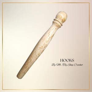 May include: A light-colored crochet hook with a rounded top and a tapered handle. The hook is made of a light-colored material with a speckled pattern. The word "HOOKS" is printed on the image, along with "By Mr. Toy Shop Crochet".