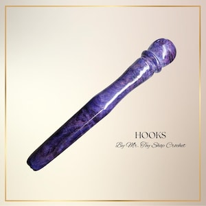May include: A handcrafted crochet hook with a purple and blue marbled design. The hook has a rounded handle and a tapered shaft. The text "HOOKS" and "By Mr. Toy Shop Crochet" are displayed in black.