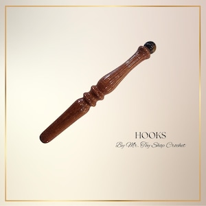 May include: A handcrafted crochet hook made of dark brown wood, featuring a decorative handle and a small, dark sphere at the top. The text "HOOKS" and "By Mr. Toy Shop Crochet" are displayed below the hook.