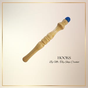 May include: A wooden crochet hook with a light brown finish and a blue tip. The hook has a detailed, carved design and the text "HOOKS By Mr. Toy Shop Crochet".