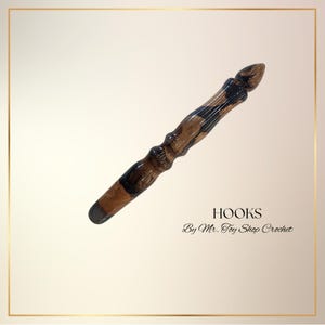 May include: A handcrafted crochet hook with a dark brown and black marbled design. The hook has a tapered end and a decorative handle. The text "HOOKS" and "By Mr. Toy Shop Crochet" are visible.