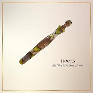 May include: A handcrafted crochet hook with a unique design. The hook features a blend of brown, green, and tan tones, with a smooth, ergonomic shape. The text "HOOKS By Mr. Toy Shop Crochet" is displayed.