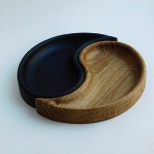 Könnte beinhalten: Ein Holztablett in Form eines Yin-Yang-Symbols. Eine Hälfte ist schwarz gebeizt, die andere Hälfte ist naturbelassen.
