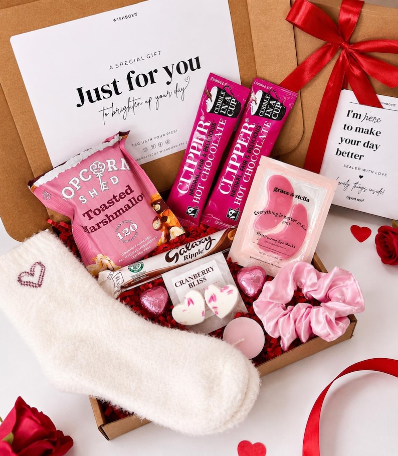May include: A gift box containing a pair of white fuzzy socks with a heart, two pink Clipper hot chocolate sachets, a bag of Popcorn Shed toasted marshmallow popcorn, a Galaxy Ripple bar, pink eye masks, heart-shaped candies, and a pink scrunchie.