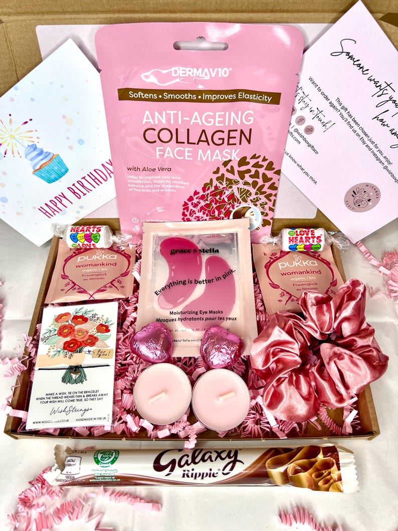 May include: A pink and brown gift box filled with various items, including a face mask, eye masks, a hair scrunchie, chocolate, candles, and a card that says "Happy Birthday".