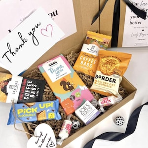 以下が含まれることがあります： コーヒーバッグ、チョコレートバー、クッキーなどのお菓子が入ったギフトボックス。黒いリボンで結ばれており、「ありがとう」と書かれたカードが付いています。