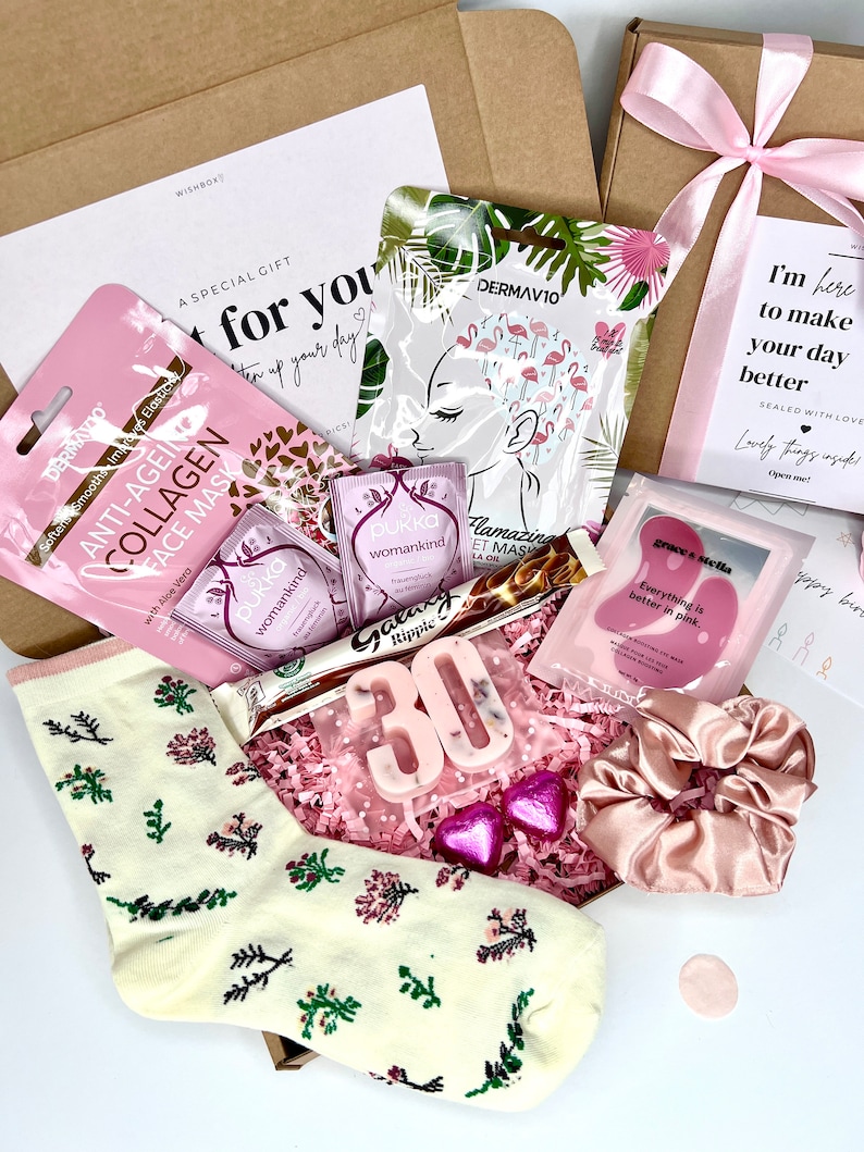 May include: A gift box containing a pair of cream socks with floral patterns, a pink satin scrunchie, two Pukka tea bags, a Galaxy Ripple chocolate bar, a number 30 candle, two heart-shaped chocolates, and three skincare face masks.