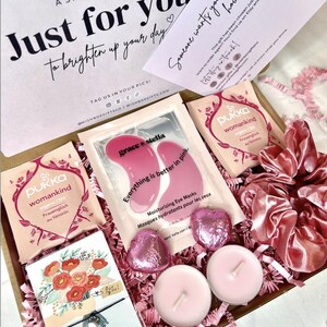 May include: A gift box containing two Pukka Womankind tea bags, a pair of Grace & Stella pink moisturizing eye masks, two heart-shaped chocolates in pink foil, two light pink tea light candles, a pink satin scrunchie, and a WishStrings bracelet.