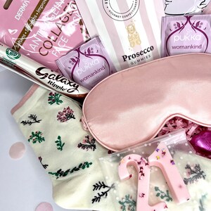 May include: A gift box containing a pink satin sleep mask, cream-colored socks with a floral pattern, a Galaxy Ripple chocolate bar, two Pukka Womankind tea bags, a Dermavive collagen face mask, Ask Mummy & Daddy Prosecco gummies, and a pink number 21.