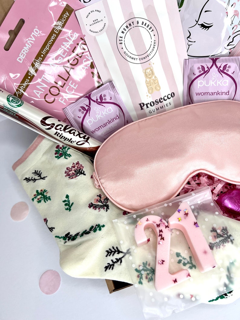 May include: A gift box containing a pink satin sleep mask, cream-colored socks with a floral pattern, a Galaxy Ripple chocolate bar, two Pukka Womankind tea bags, a Dermavive collagen face mask, Ask Mummy & Daddy Prosecco gummies, and a pink number 21.