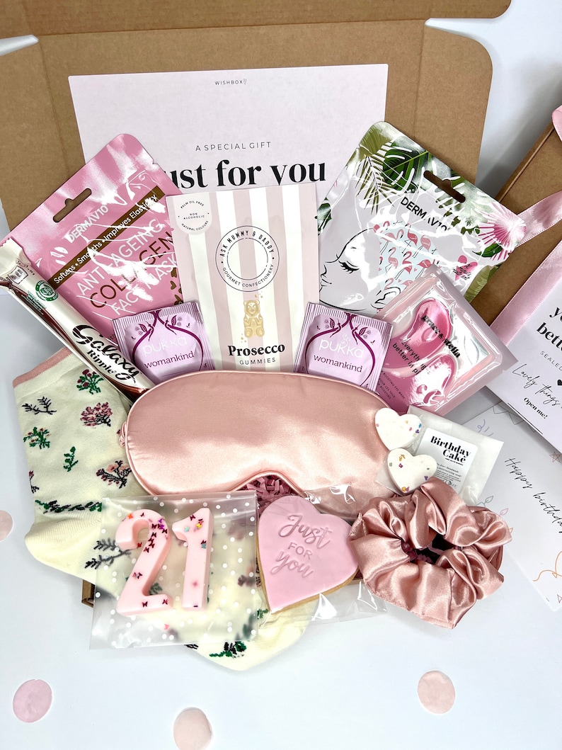 May include: A gift box containing a pink satin sleep mask, a matching pink scrunchie, a pair of cream socks with floral patterns, two Pukka tea bags, a Dermavio face mask, Prosecco gummies, a heart-shaped cookie, and a number 21 candle.
