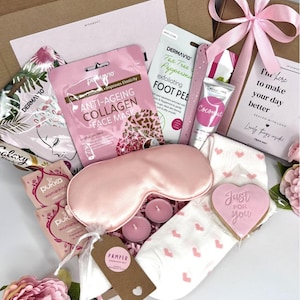 Könnte beinhalten: Eine Geschenkbox mit Pflegeprodukten, darunter eine rosa Augenmaske, Gesichtsmasken, Fußpeeling, Kokosnusscreme, Socken mit rosa Herzen, Kerzen und ein herzförmiger Keks mit der Aufschrift "Just for you".
