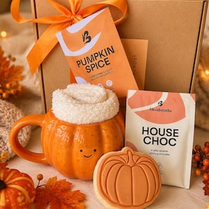 May include: A gift box tied with an orange ribbon containing a pumpkin-shaped orange mug with a white fuzzy sock inside, a packet of Pumpkin Spice blend, a packet of House Choc drinking chocolate, and a round cookie with a pumpkin design.