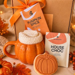 May include: A gift box tied with an orange ribbon containing a packet of Pumpkin Spice, a packet of House Choc, a white fuzzy sock inside an orange pumpkin-shaped ceramic mug, and a round cookie with a pumpkin design embossed on the surface.