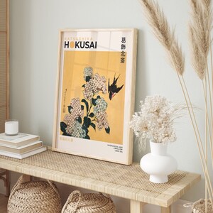May include: A framed print of a Japanese woodblock print by Katsushika Hokusai, depicting hydrangeas and a swallow. The print is titled "Hydrangeas and Swallow (1832-34)" and is in a light wood frame.
