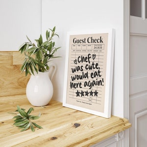 May include: A framed guest check with a handwritten message that reads "Chef was cute, would eat here again!" with five stars for a rating. The check is on a light brown background with black lines and text.